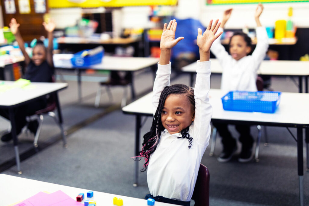 ACCEL School students raise their hands over their heads in a classroom
